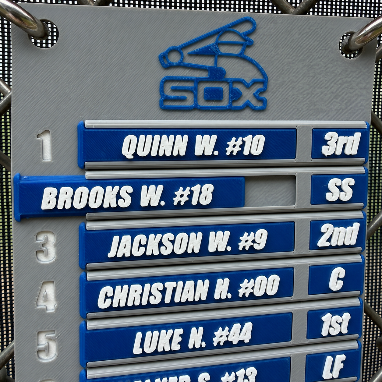 Gray and blue 4LifeTags custom baseball lineup board hanging on a fence