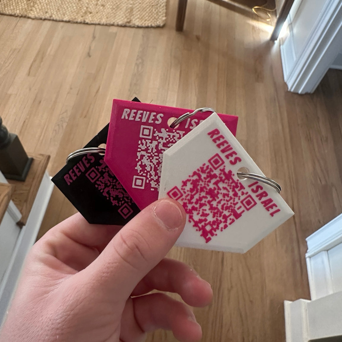 Hand holding multiple Reeves art supply tags with QR codes on a wooden floor background