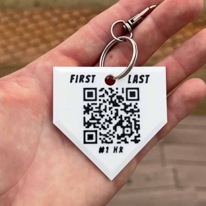 Hand holding a keychain with a QR code and customizable text on a blurred background
